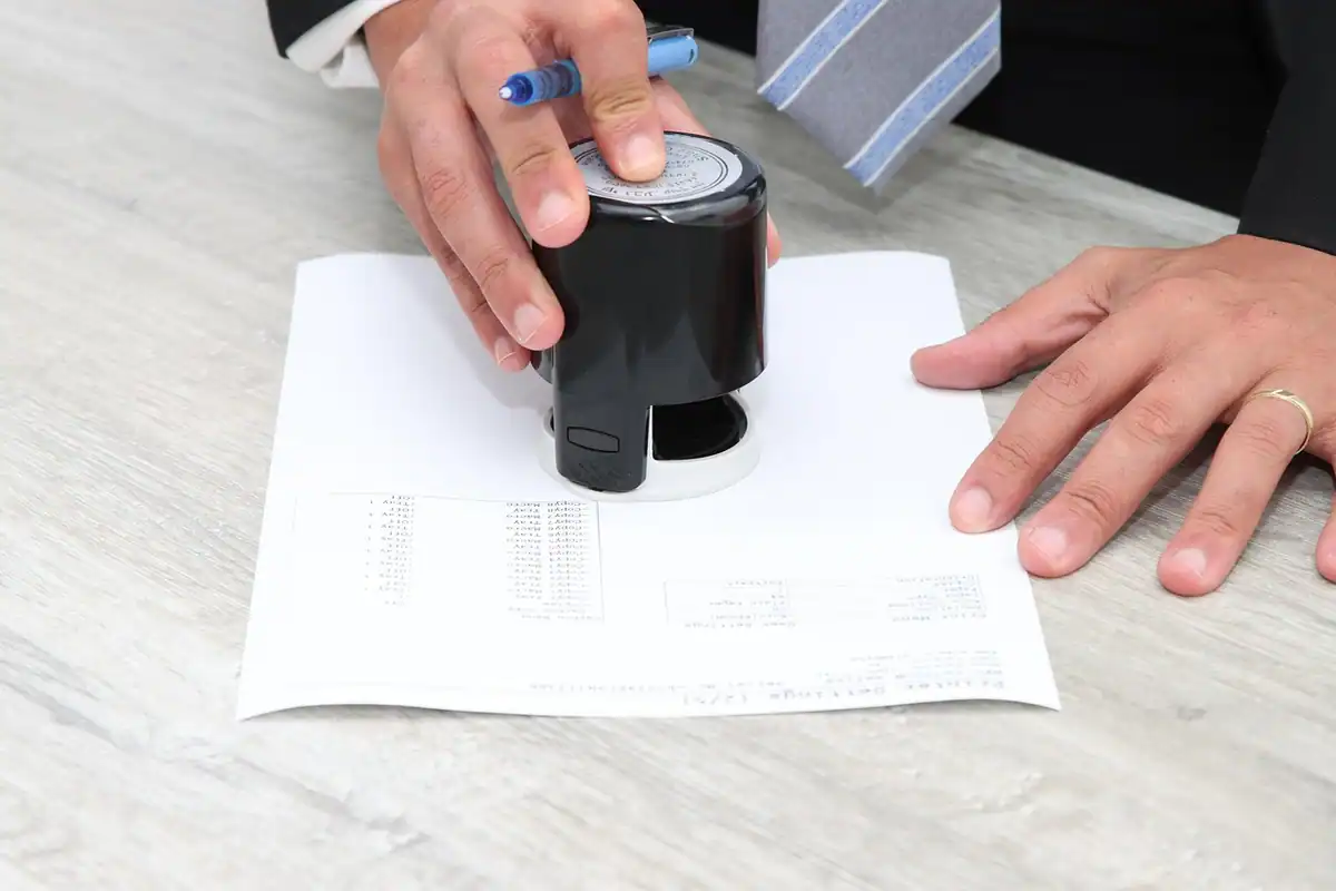 Mână care aplică ștampila rotundă pe un document oficial, ca la eliberarea certificatului de atestare fiscală