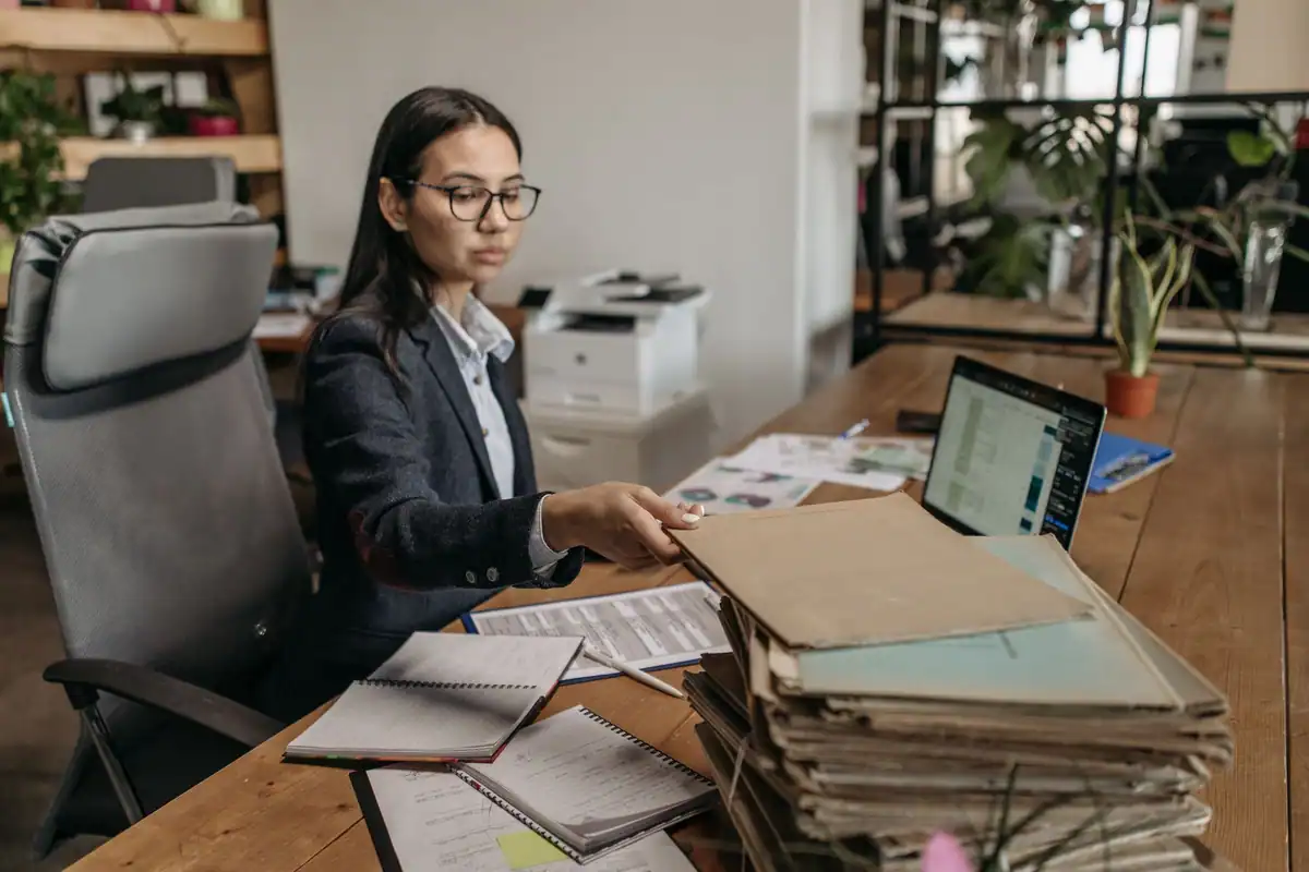 Femeie la un birou din lemn, cu documente și laptop, într-un birou modern