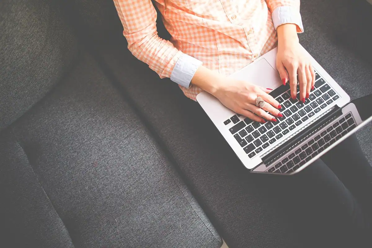 Mâini care tastează pe un laptop așezat pe genunchi, la pregătirea unei facturi pentru e-Factura