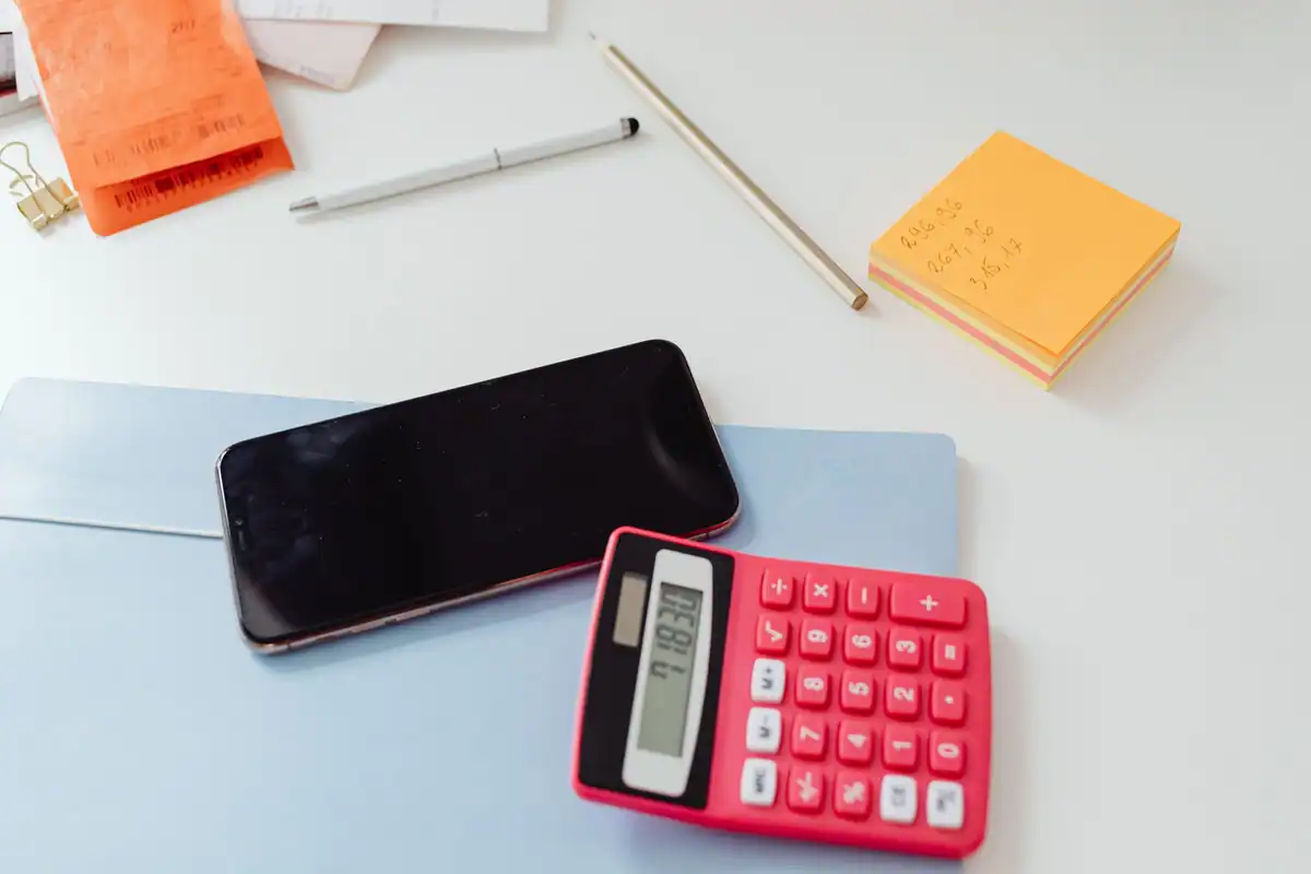 Birou alb cu telefon, calculator roșu și notițe adezive, la calculul contribuțiilor din statul de plată
