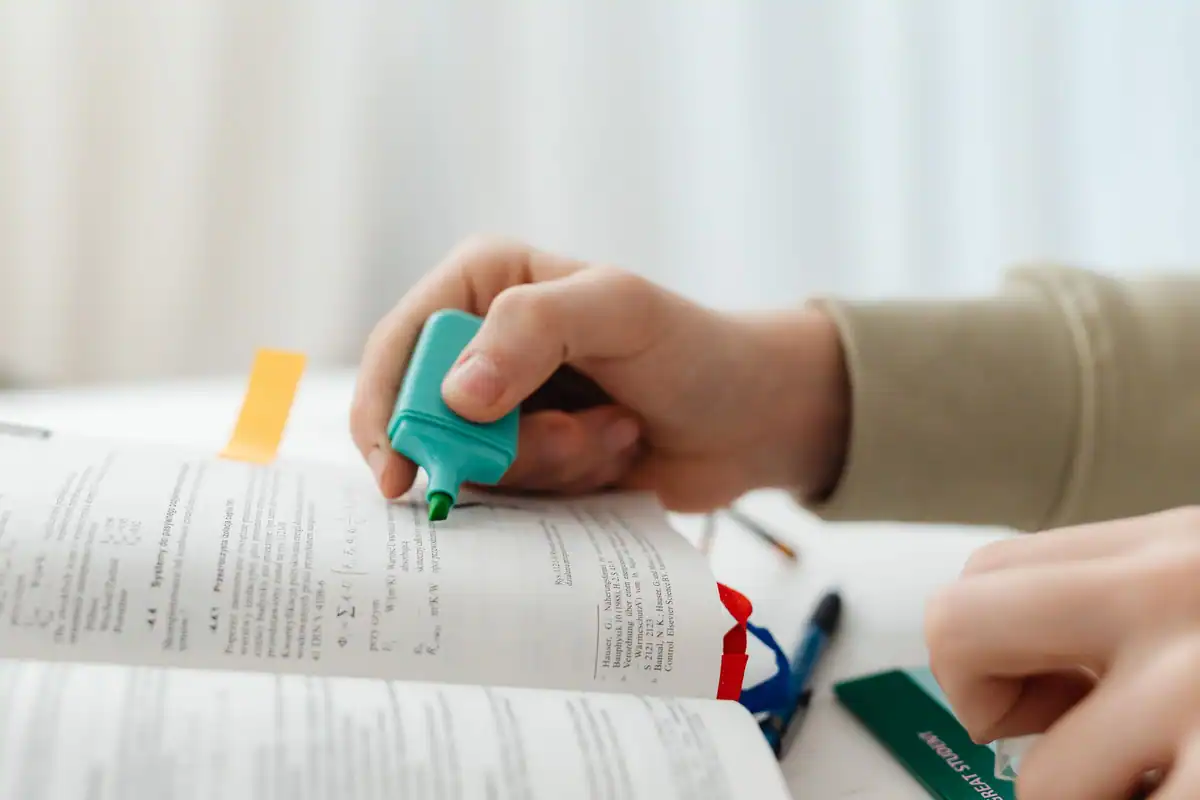 Mână care evidențiază cu markerul verde un rând dintr-o carte, la corectarea unei declarații fiscale
