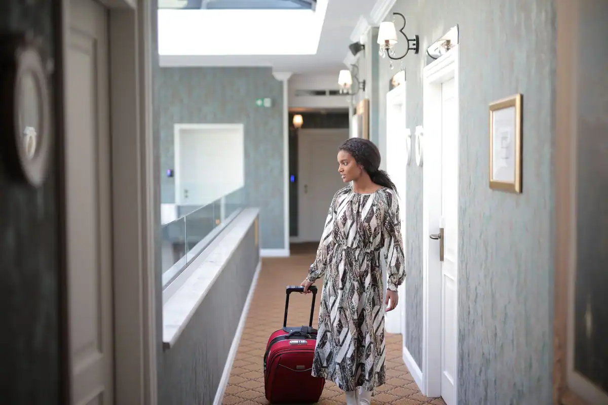 Femeie care merge pe un coridor de hotel, trăgând un geamantan, într-o deplasare de serviciu