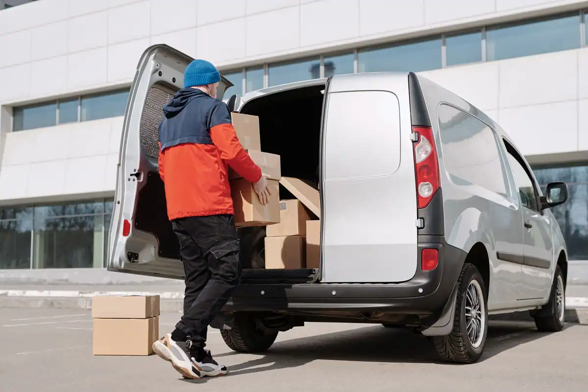 Curier în geacă portocalie care scoate cutii dintr-o dubă albă, ca la transportul declarat în e-Transport