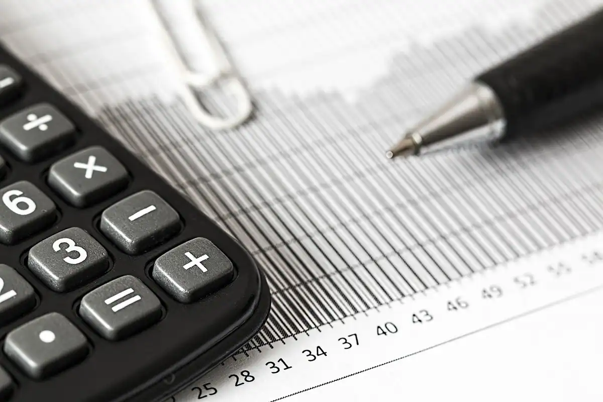 Contabil care calculează cu un calculator mic, lângă un dosar și un laptop, impozitul firmei