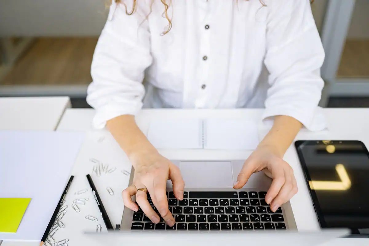 Mâini de femeie care tastează pe laptop, la un birou luminos, calculând venitul microîntreprinderii