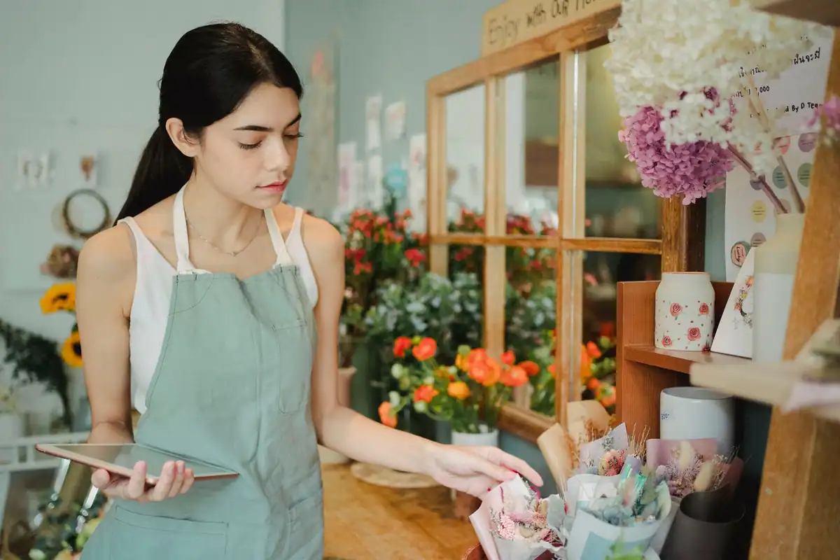 Florăreasă într-un magazin cu flori, ținând o tabletă în mână, la verificarea încasărilor