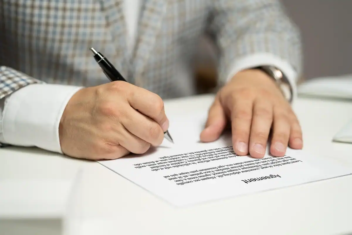 Mâini care semnează un document pe masă, cu pixul în mână, la schimbarea regimului de impozitare