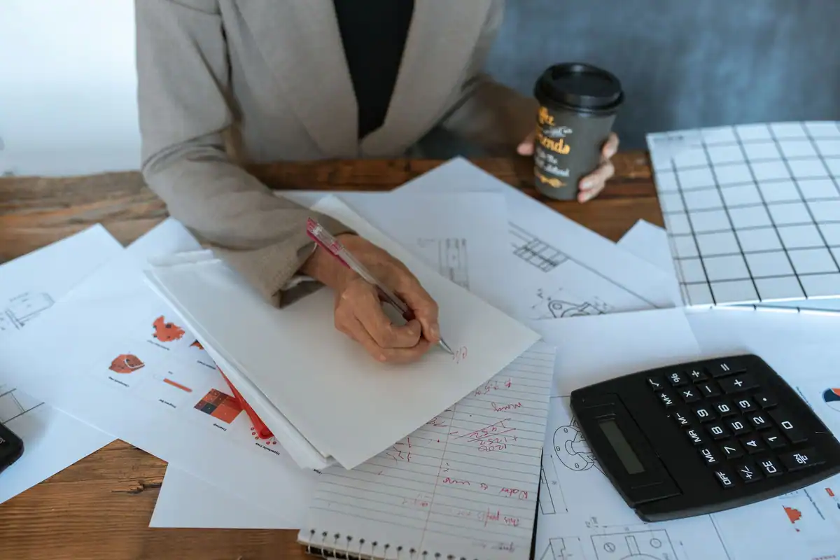Mână care scrie pe foi, lângă calculator și o cană de cafea, la vectorul fiscal